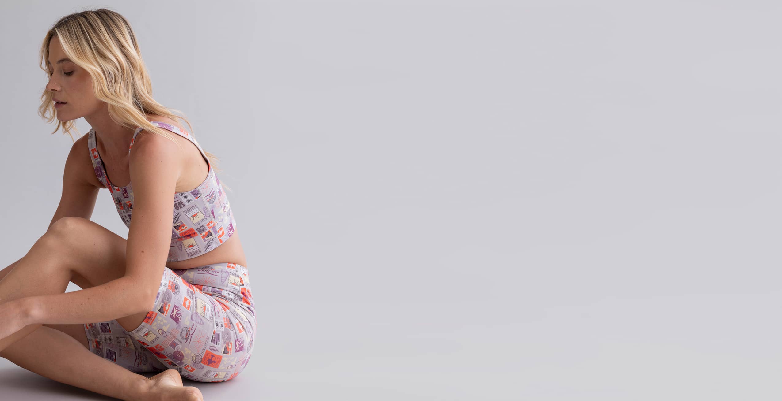 Hey Honey woman in a lilac patterned crop top and matching shorts, sitting on a light background.