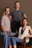 Three women of Hey Honey, two seated in jeans and sweaters, one standing in a grey tee and black jeans.