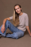 Hey Honey model in light wash jeans and a beige short-sleeve knit top, sitting on a brown background.