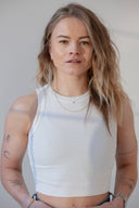 Young woman with blonde hair, wearing a white ribbed tank top and gold necklace. Hey Honey.