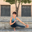 Hey Honey woman in teal top and dark leggings doing a yoga pose outdoors, with a tree and buildings in background.